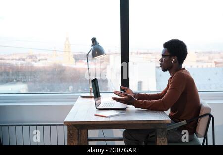 African young man sitting at the table and using laptop for online meeting at office Stock Photo