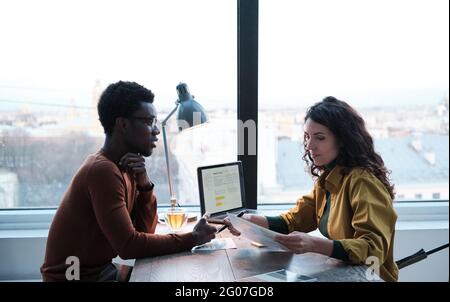 Young businesswoman sitting at the table with laptop and examining the documents while holding business interview Stock Photo