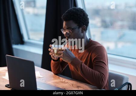 African businessman drinking coffee while sitting at the table and working on laptop Stock Photo