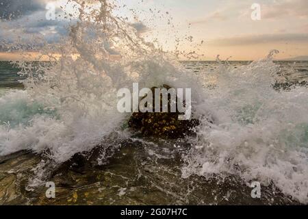 A Wave Is Breaking And Splashing On Sea Rocks As Ocean Spray Is Captured In Mid Air Stock Photo