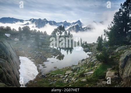 Aigüestortes National Park summits, in Pyrenees, in a summer foggy sunrise, seen from a lake near the Amitges mountain hut (Pallars Sobirà, Cataluña) Stock Photo