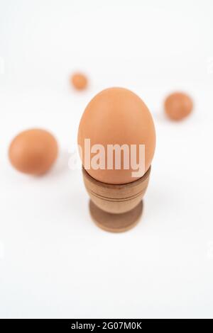 Wide angle vertical shot of hen egg in old wooden egg stand isolated on white background with three more eggs in the back. Conceptual art for egg-rela Stock Photo