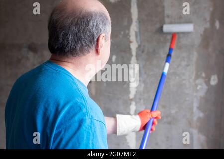 Man painting cement walls using roller brush and primer making a renovation. Stock Photo