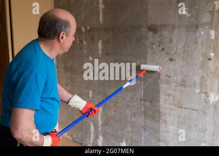 Man painting cement walls using roller brush and primer making a renovation. Stock Photo