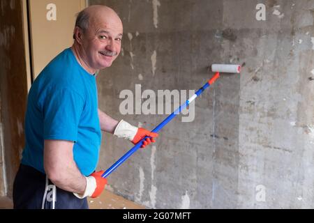 Man painting cement walls using roller brush and primer making a renovation. Stock Photo