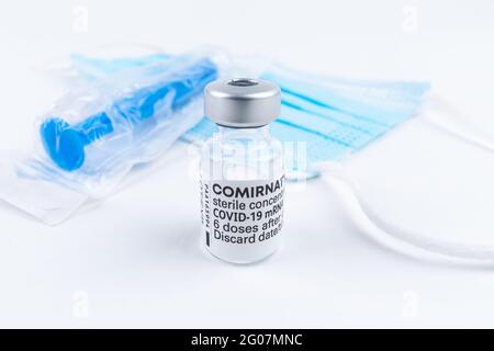 Celadna, Czechia - 05.30.2021: Still life with ampoule of Comirnaty vaccine by Pfizer, blue face mask and blue syringe on white background. Stock Photo