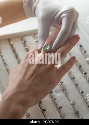 A client of a jewelry store tries on a silver ring with a natural stone. Female hand in a white glove. Stock Photo