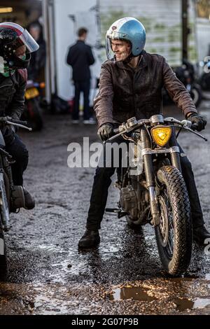 man dressed in jeans and leather jacket with motorcycle talking to friend. Stock Photo