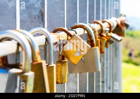 Padlock with two hearts in a row of rusty old closed locks on the fence of the bridge. Tractional love custom. Colorful summer view Stock Photo