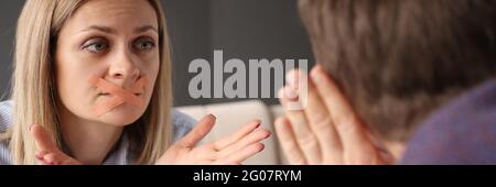 Young woman with sealed mouth showing gestures to man Stock Photo