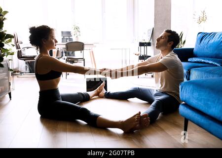 Sporty young couple warming up stretching watching fitness video tutorial online on laptop, fit man and woman doing workout at home sitting on floor Stock Photo