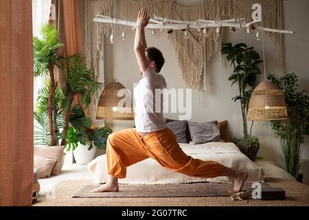 man practicing yoga doing warrior pose or virabhadrasana at home Stock Photo