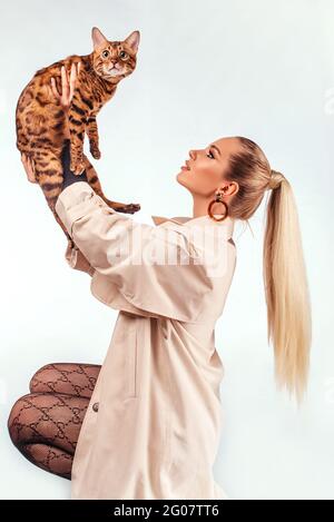 Cute blonde girl posing in the studio. Beautiful blue eyes. Girl with Bengal cat. Beauty, fashion. Photo Catalog. Portrait of a young girl. Girl with Stock Photo