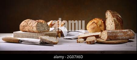 Various sizes of traditional bread with cutting boards and knife on rustic wooden table, space for text, panoramic horizontal format. Stock Photo