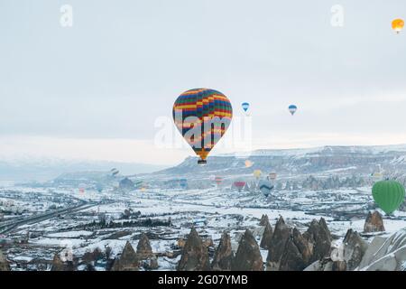 Multicolored air balloons n cloudy sky over ancient settlement with stone and cave houses against foggy highland in overcast weather in Turkey Stock Photo