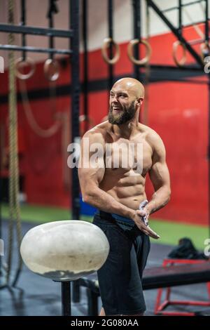 Muscular bearded man in sportswear clapping hands and spreading powder during bodybuilding workout in gym Stock Photo