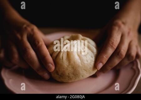 Hands of middle aged Woman putting steamed baozi bun on ceramic plate Stock Photo