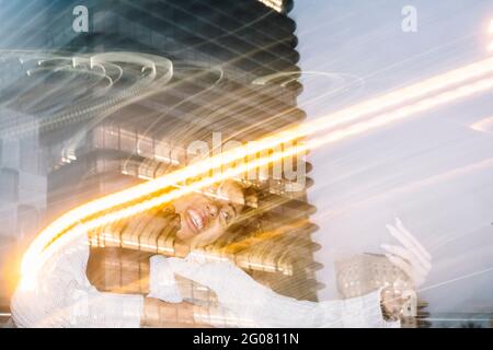 Unrecognizable cheerful black guy in stylish outfit giving piggyback ride to happy girlfriend taking selfie on mobile phone near freeze lights on stre Stock Photo