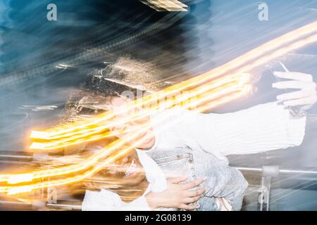 Unrecognizable cheerful black guy in stylish outfit giving piggyback ride to happy girlfriend taking selfie on mobile phone near freeze lights on stre Stock Photo