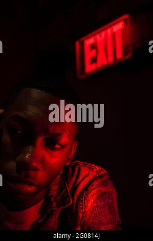 African American young male looking away near a illuminated tablet Exit above head in red dark light Stock Photo