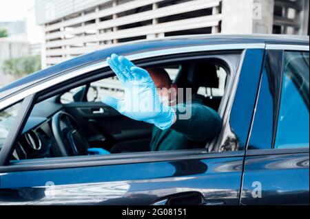 Side view of serious man using a protective mask driving car during quarantine time making top gesture with hand looking at camera Stock Photo