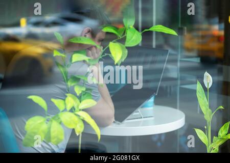 Behind windowpane of a cafe young man working at laptop. Soft focus. Light bokeh. Modern technology. Regular people out in public places Stock Photo