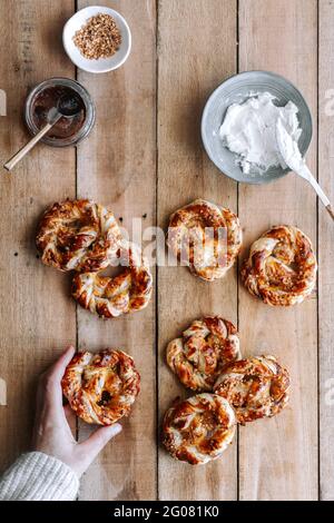 Top view of unrecognizable person taking delicious pretzel with fig jam and cream cheese from lumber table in kitchen Stock Photo