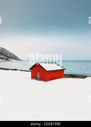 Red shack located on white snowy coast of sea against cloudless blue sky on Lofoten Islands, Norway Stock Photo