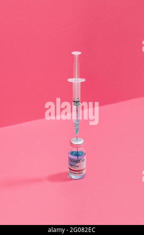 Coronavirus vaccine flask near syringe with needle on pink background Stock Photo