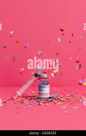 Coronavirus vaccine flask near syringe with needle on pink background covered with confetti Stock Photo