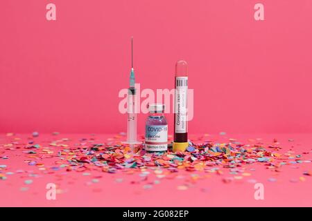 Coronavirus vaccine flask near blood test and syringe on pink background covered with confetti Stock Photo