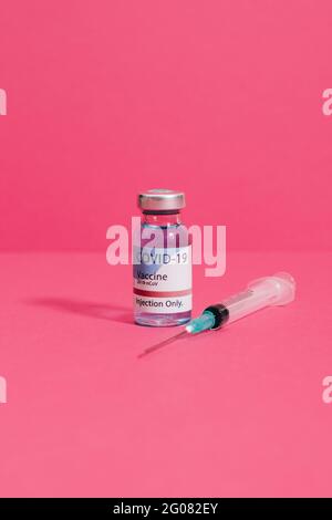 Coronavirus vaccine flask near syringe with needle on pink background Stock Photo