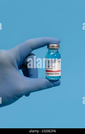 Cropped unrecognizable doctor's hand holding showing coronavirus vaccine flask on blue background Stock Photo