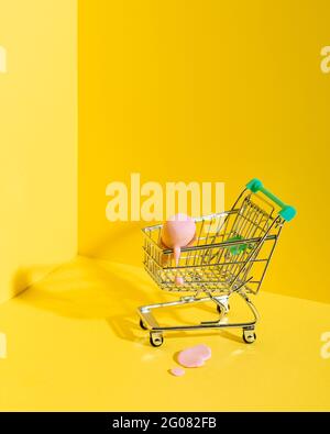 From above composition of miniature shopping trolley with assorted multicolored ice cream cones placed near fallen melting blue ice cream on yellow ba Stock Photo