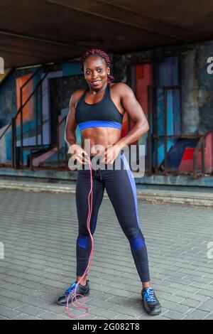 Muscular African-American sportsWoman standing with jumping rope and smiling on street Stock Photo