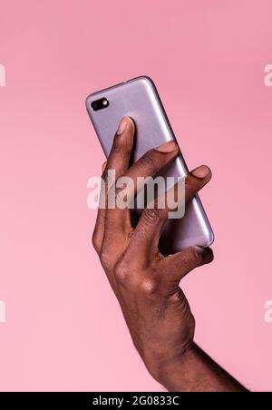 Crop hands of african american man holding phone and doing gesture isolated on pink background Stock Photo