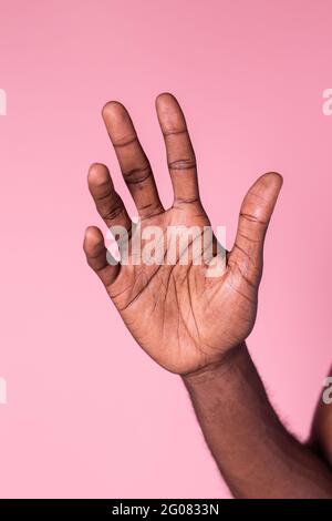 Crop forearm of african-american man raising hand against pink background Stock Photo