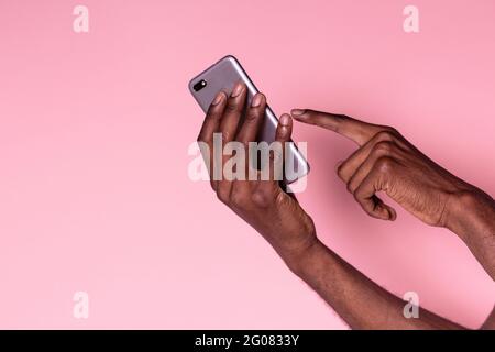 Crop hands of african american man holding phone and doing gesture isolated on pink background Stock Photo