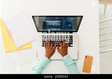Top view of crop black female typing on laptop keyboard while working at white table with documents Stock Photo