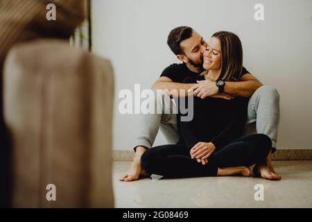 Smiling female embracing and kissing cheerful man in forehead while sitting on floor Stock Photo