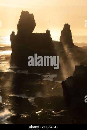 Bright beams of rising sun shining through rough rock over magnificent stormy sea in morning in Iceland Stock Photo