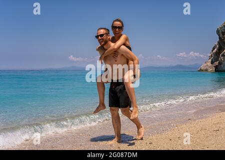 Young man carrying girlfriend on his back along the beach Stock Photo