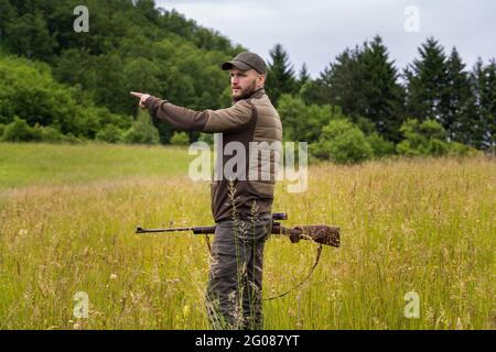 Young hunter pointing a direction with his hand while holding a sniper rifle Stock Photo