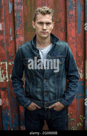 Handsome man wearing denim jacket with weathered red metal background Stock Photo
