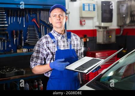 Mechanic man using laptop checking car in workshop Stock Photo