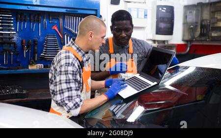 Two auto mechanics diagnosing car engine with laptop Stock Photo