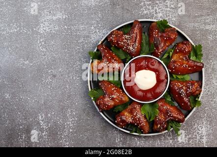 Baked chicken wings with sesame and sauce on a round plate on a dark background. Top view, flat lay Stock Photo