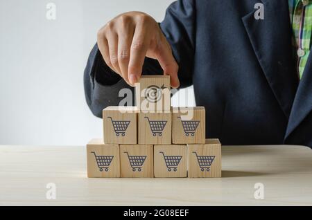 Hand holding wood cube with icon goal and shopping cart symbol.Increased sales volumes make the business successful. Stock Photo