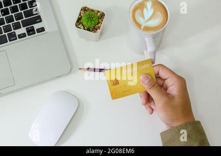 Top view man holding a credit card and on the desk. Laptop computer Notepad and pen.Online shopping business, pay by credit card. Stock Photo