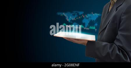Stock market trading concept with a digital tablet  businessmen holding hand on virtual screen. Business finance and graph with world map on dark back Stock Photo